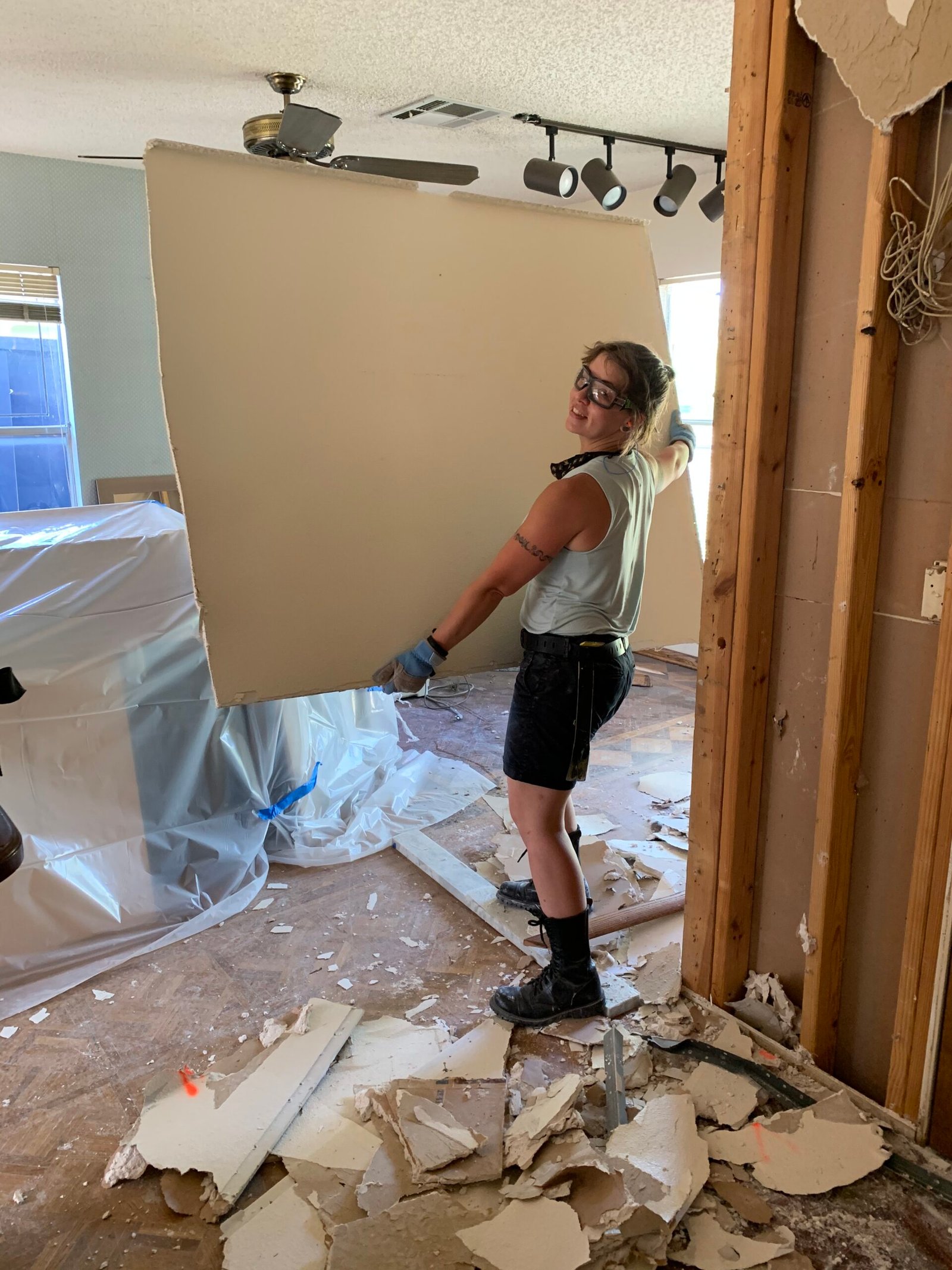 Robin Horal wears work boots as she carries a piece of plywood through a house mid-construction