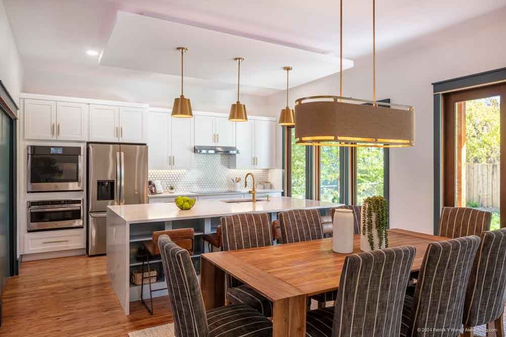 Kitchen with white island, gold linear pendant light, and dark cabinetry