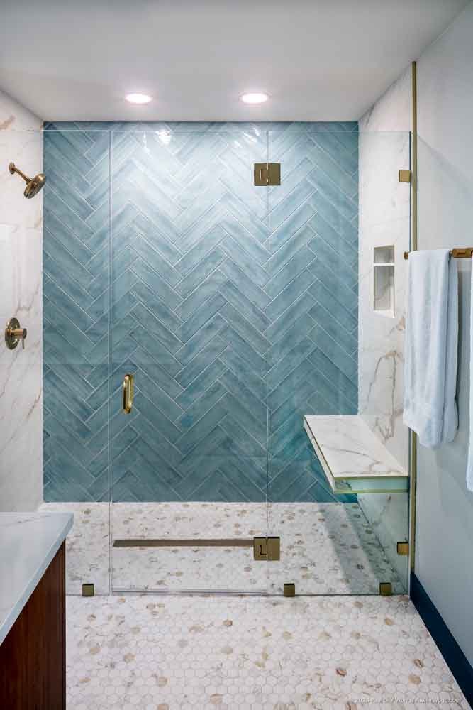 Walk-in shower with blue chevron tile, marble bench, and gold fixtures