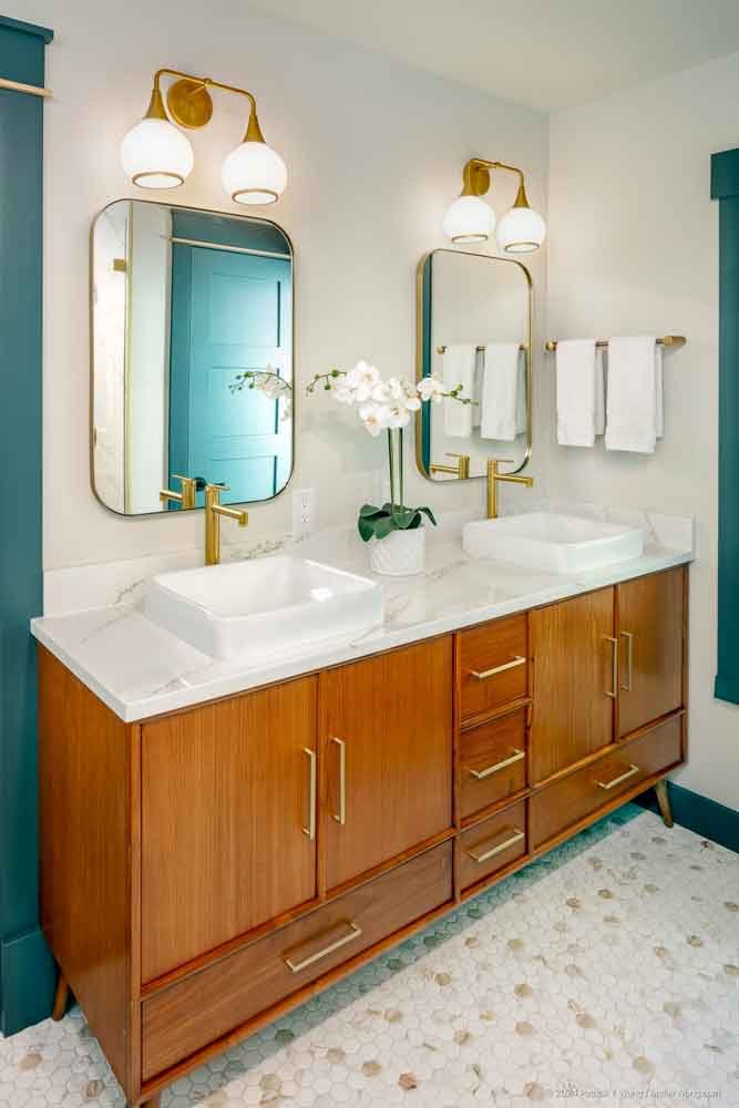 Bathroom with dual wood vanity, marble-look countertop, oval mirrors, and gold fixtures