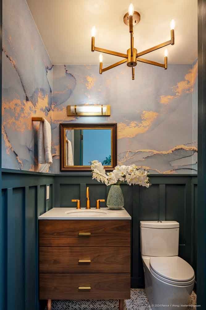 Powder room with dark green board-and-batten walls, wood vanity, gold fixtures, and marbled wallpaper
