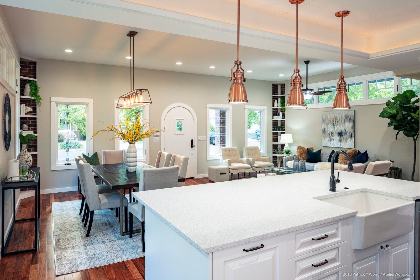 Open-concept dining and kitchen with white waterfall island, arched doorways, and copper pendant lights